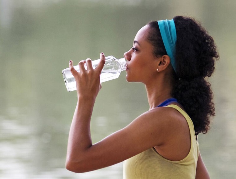 woman drinking from glass water bottle 