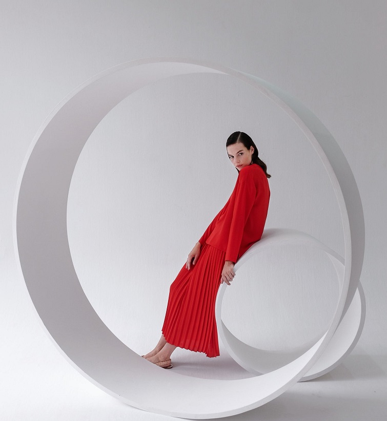 picture of a woman in red dress standing beside circle sculpture with white background 