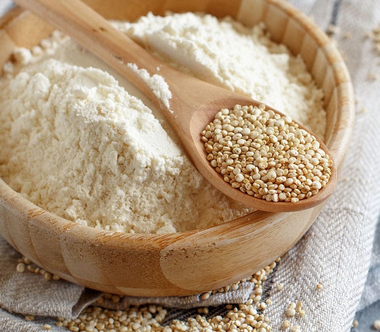 Quinoa flour and quinoa grains in wooden spoon close up 