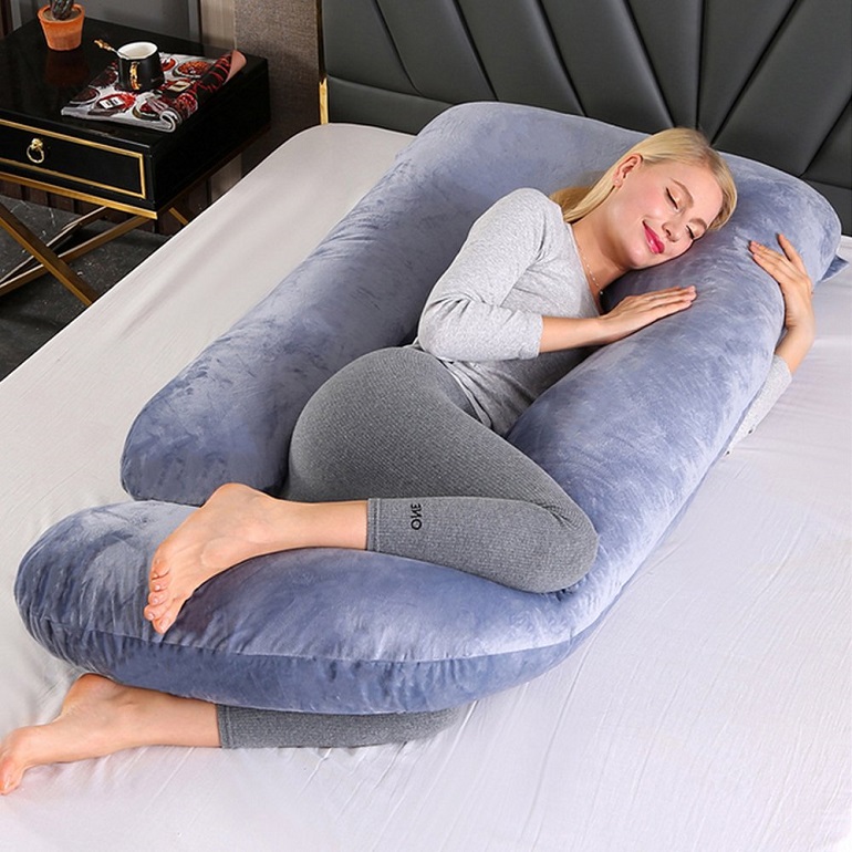 picture of a woman on a bed beside a maternity pillow 